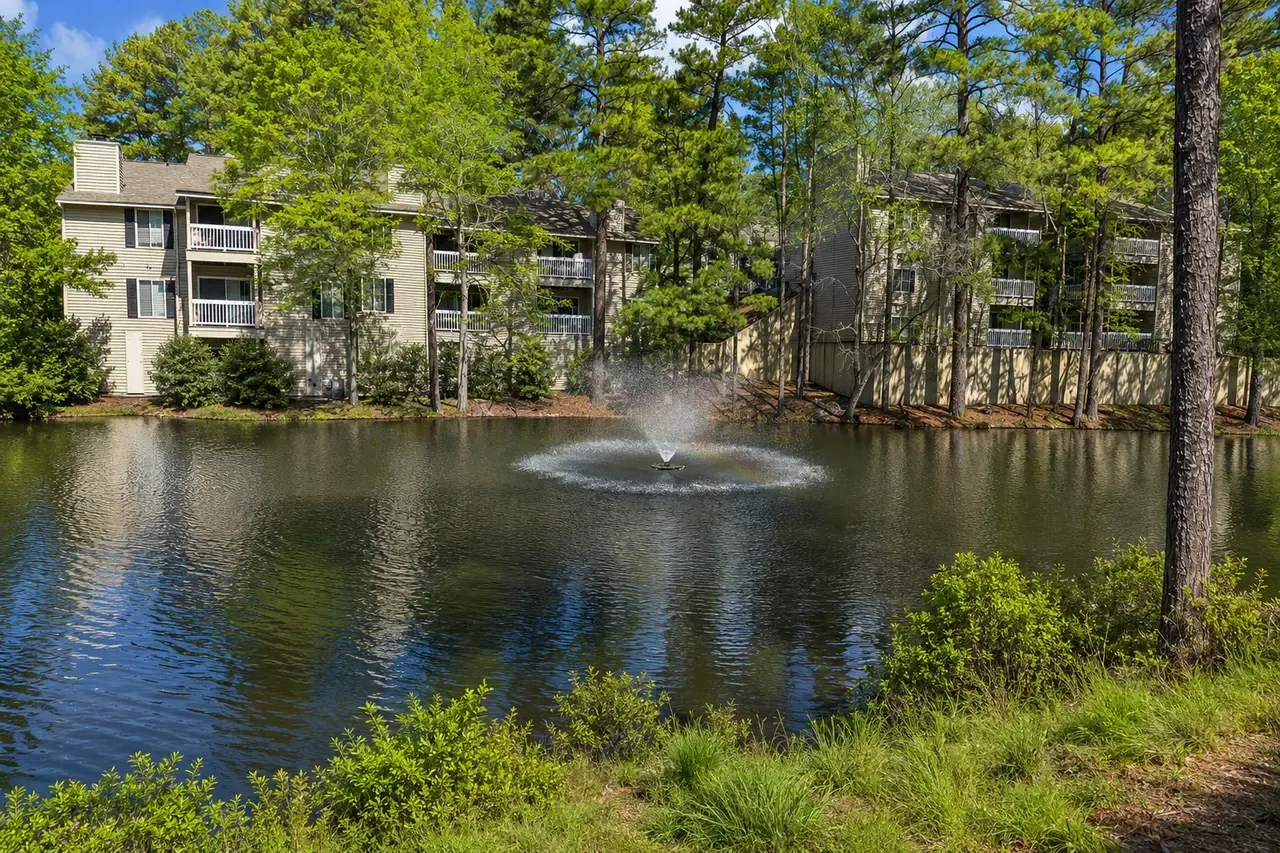 The pond and fountain at The Woods at Windy Hill, with apartment buildings among tall pines